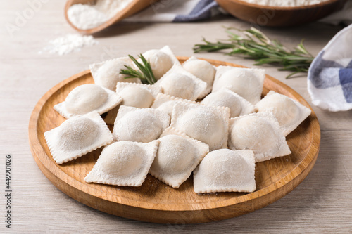 Uncooked ravioli and rosemary on white wooden table