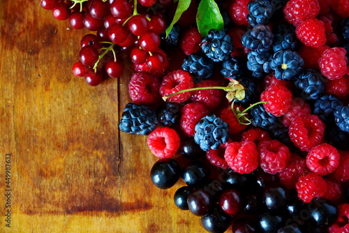 Black and red summer berries still-life. Mix berries bramble, blackberry, cherries, bunch red bird cherry and red raspberries on old wooden table. Top view with copy space
