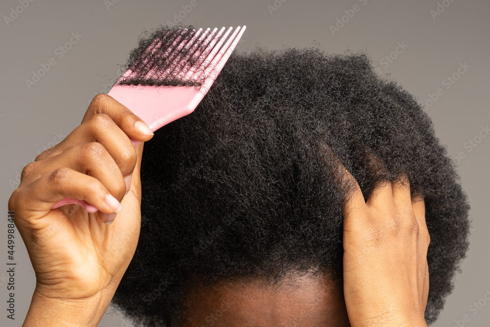 Close up of African American woman using pink plastic comb over studio gray wall background. Unrecognizable black girl brushing curly trick hair, Haircare, daily routine concept. - obrazy, fototapety, plakaty 