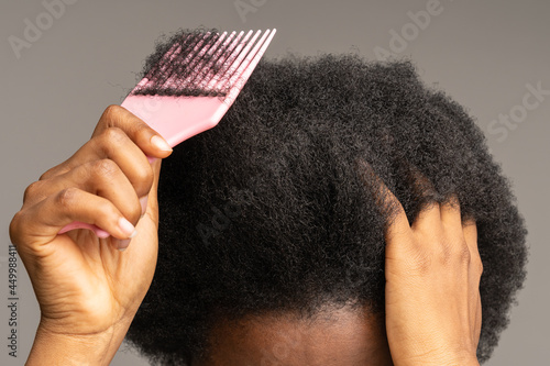 Close up of African American woman using pink plastic comb over studio gray wall background. Unrecognizable black girl brushing curly trick hair, Haircare, daily routine concept. photo