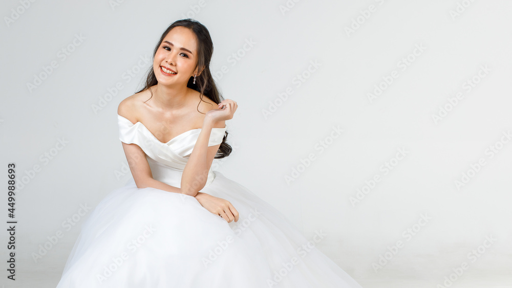 Young attractive Asian woman, soon to be bride, wearing white wedding gown sitting down looking happy. Concept for pre wedding photography Young attractive Asian woman, soon to be bride, wearing white wedding gown sitting down looking happy. Concept for pre wedding photography