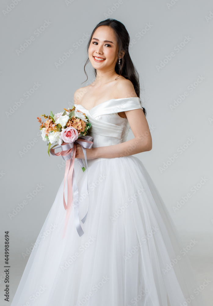 Young attractive Asian woman, soon to be bride, wearing white wedding gown looking happy holding bouquet of flower. Concept for pre wedding photography Young attractive Asian woman, soon to be bride, wearing white wedding gown looking happy holding bouquet of flower. Concept for pre wedding photography