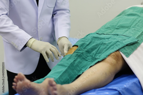Doctor wear white gown, Inject anesthetic to patient's knee  for prepare surgery. photo