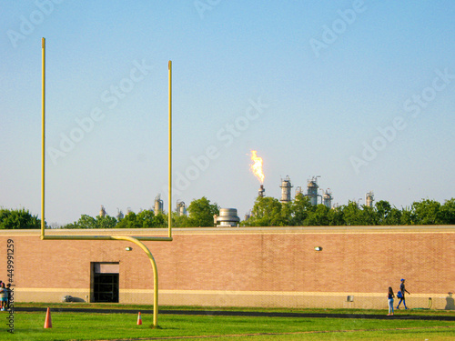 Refinery flare near high school football practice field in Houston, Texas Refinery flaring behind school as students ready for sports teams practices. Student on field. Houston, Texas, US. fire, air p