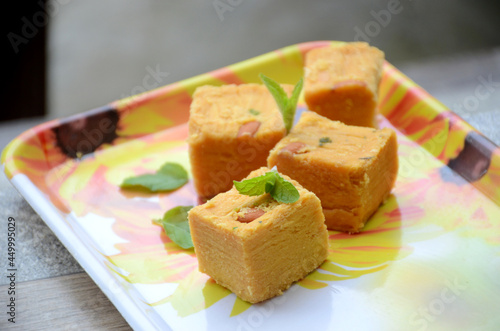 closeup the yellow gram flour sweet with green mint over out of focus yellow brown background.