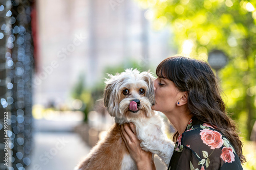 a woman holding and kissing her small mixed breed dog