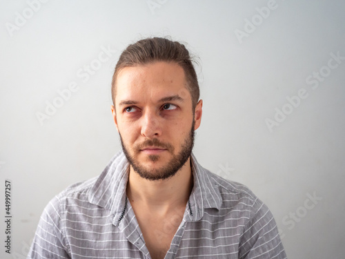 Young Caucasian Male in Grey Shirt Stares Angrily against White Background
