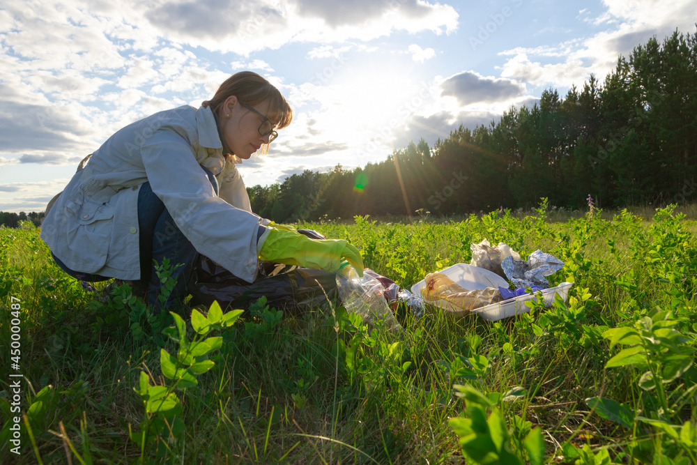 Young woman in rubber gloves on nature collects plastic garbage on a summer sunny day against the background of trees. Environmental Protection. Selective focus Young woman in rubber gloves on nature collects plastic garbage on a summer sunny day against the background of trees. Environmental Protection. Selective focus