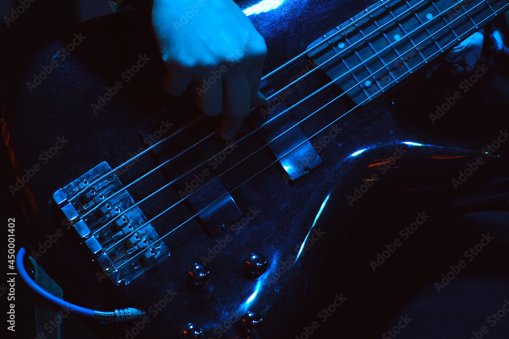 The bass player plays on black five-string bass guitar in the spotlight. Selective focus - obrazy, fototapety, plakaty 