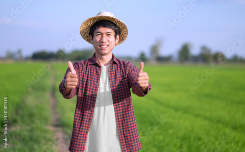 A male farmer in a striped shirt is standing smiling with two thumbs up in a green field. Selective focus on face image.