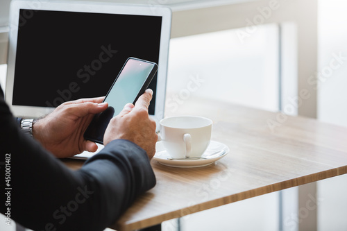 Close-up male hands using smartphone with laptop in cafe. chatting