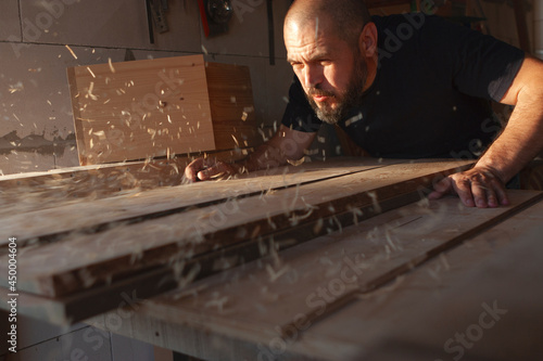 A carpenter blows sawdust off a board