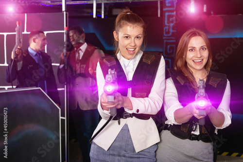 Portrait of two smiling cheerful women in business suits playing laser tag with co-workers © JackF