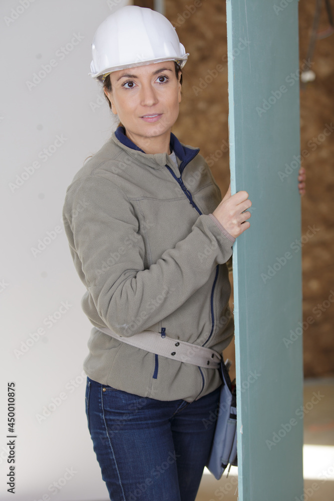 female builder carrying sheet of plasterboard female builder carrying sheet of plasterboard