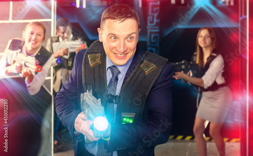 Cheery man and his colleagues on background having corporative entertainment in laser tag room