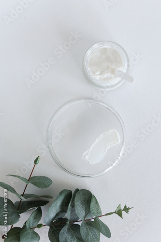 Moisturizing cosmetic cream with eucalyptus stands on neutral background with milk splash