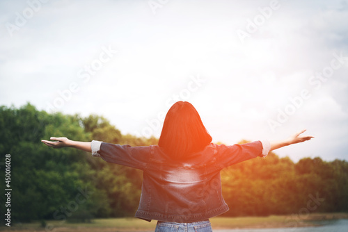 Young woman open arms out to see the sunrise on the top of the mountain with the bright weather in the forest with a bright relaxing atmosphere concept for religion prayer and praise.