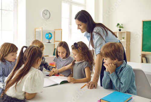 Group of children looking at picture that little girl is showing. Happy school teacher and students have interesting classes, learn, discuss new things, work on creative projects in modern classroom