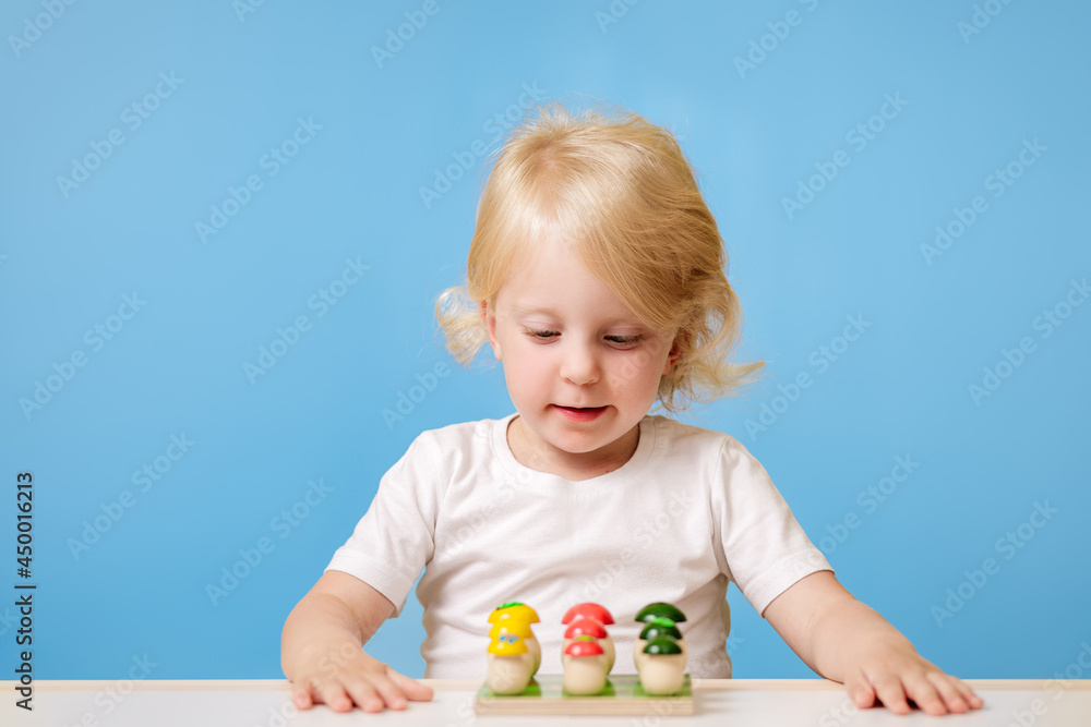 A 3-year-old child is playing at a table with a colorful education toy on blue background A 3-year-old child is playing at a table with a colorful education toy on blue background
