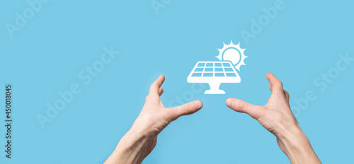 Hand on a blue background holds the icon symbol of solar panels. Renewable energy, solar panels station concept, green electricity