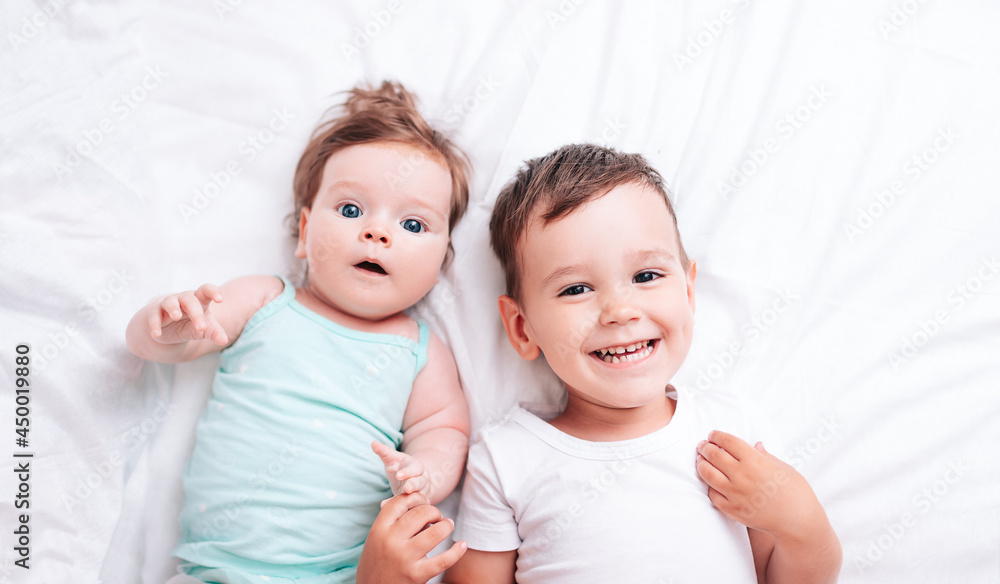 happy little brother hugs his little sister lying on a white blanket happy little brother hugs his little sister lying on a white blanket