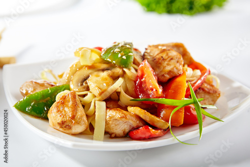 Udon noodles with sweet and sour chicken and vegetable. Asian style noodles food on white background. Udon in white plate with wooden choopsticks.