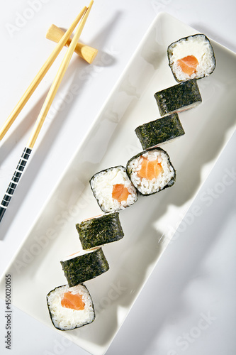 Philadelphia Sushi Roll made with Smoked Salmon. Maki sushi with nori seaweed outside, salmon and cream cheese inside. White plate with wooden chopsticks on white table. photo