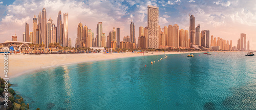 Cityscape panorama of the golden sand illuminated by the setting sun in the JBR beach area. Amazing skyscrapers and azure waters of the Persian Gulf are waiting for visitors