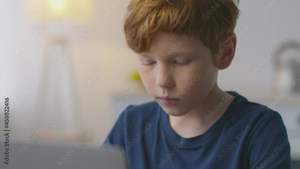 Close up portrait of cute little redhead boy typing on laptop at home, studying foreign language distantly, slow motion Close up portrait of cute little redhead boy typing on laptop at home, studying foreign language distantly, slow motion