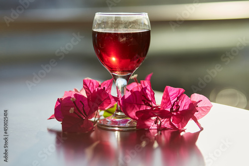 Glass of red wine on blurred mountain background. Decorations of pink bougainvillea flowers. Blue hour photography