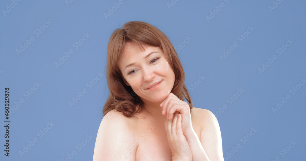 Beautiful cheerful mature woman applies skin care product, spa and wellness concept. Woman applying anti-age cream on her skin isolated on blue background. Beautiful cheerful mature woman applies skin care product, spa and wellness concept. Woman applying anti-age cream on her skin isolated on blue background.