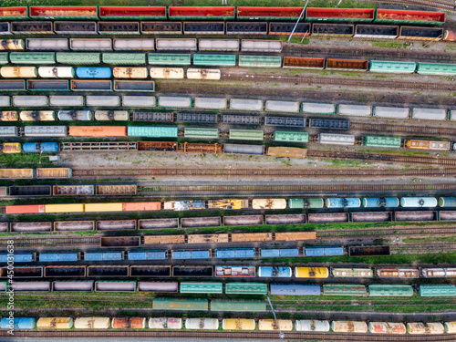 Top view on lots of various wagons: tanks, platforms, dump trucks staying on railways at depot. Cargo transportation of various goods by rail. Import and export logistics. Industrial aerial landscape.