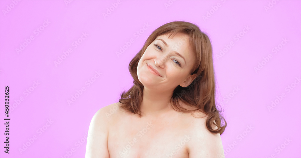 Charming mature lady smiling at camera. Beautifull woman with bare shoulders and natural makeup on pink background. Studio portrait. Skincare concept.