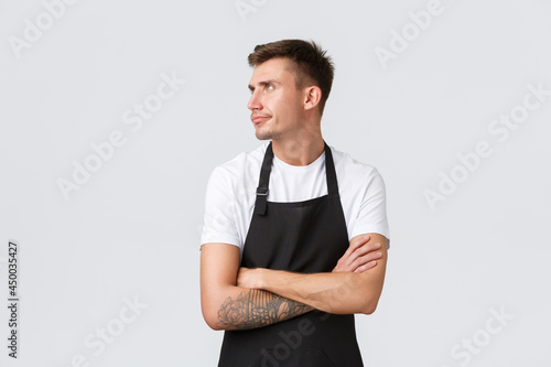 Employees, grocery stores and coffee shop concept. Displeased grumpy barista, cafe worker in black apron feeling mad or offended, turn away sulking and cross arms chest, white background photo