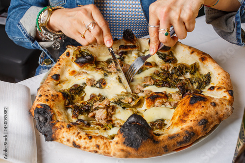 Pizza napoletana con salsiccia e friarielli mentre viene tagliata da un cliente con forchetta e coltello photo