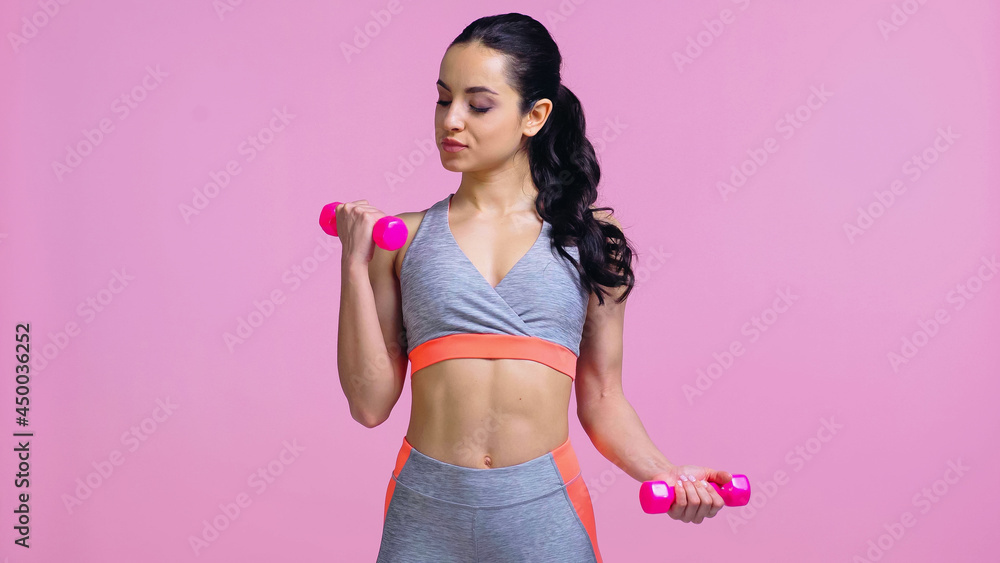 brunette sportswoman working out with dumbbells isolated on pink brunette sportswoman working out with dumbbells isolated on pink