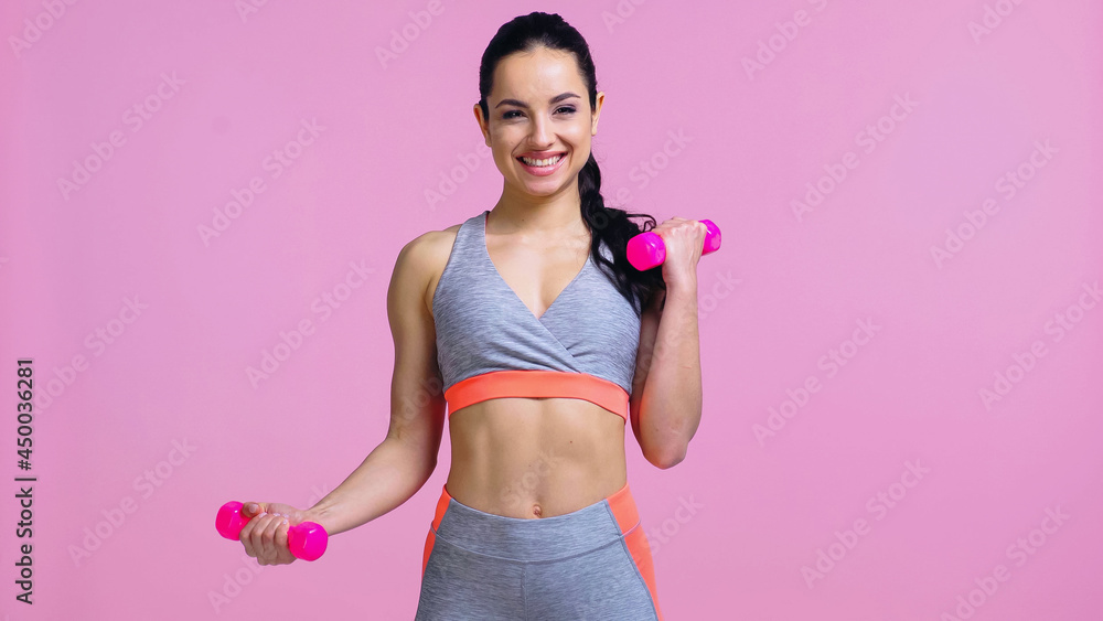 cheerful sportswoman working out with dumbbells isolated on pink cheerful sportswoman working out with dumbbells isolated on pink