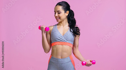 Fototapeta Naklejka Na Ścianę i Meble -  happy sportswoman working out with dumbbells isolated on pink