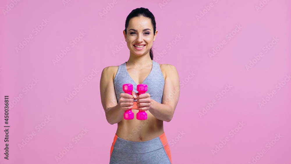 Obraz premium smiling young woman working out with dumbbells isolated on pink