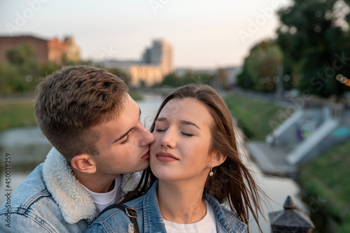 Portrait of beautiful young couple. Guy gently kissing his beloved. Happy girl closed eyes. Romantic date in city