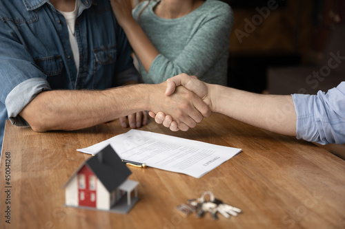 Couple of customers and real estate broker giving handshakes in office. Married clients meeting with agent, consultant, seller, lawyer, shaking hands over buying contract, toy house and keys
