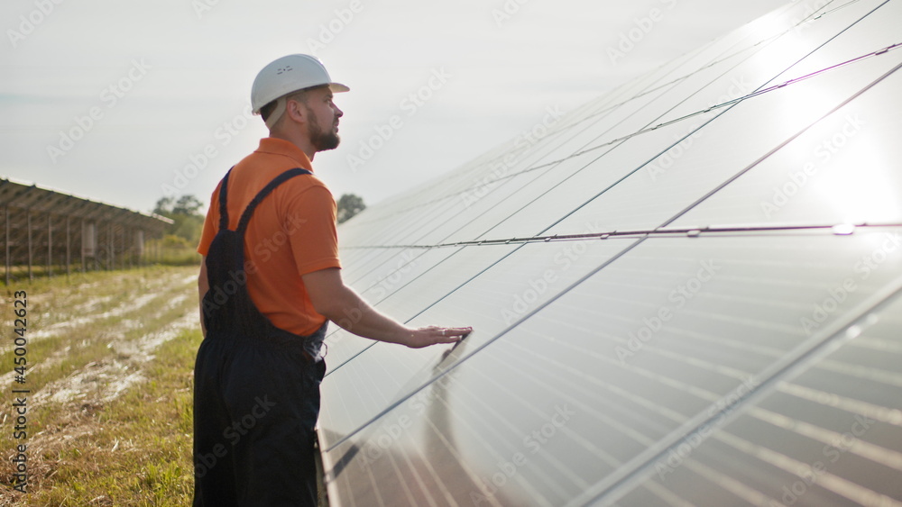 Professional male engineer in protective helmet walk on ecological solar plant construction. Concept of electricity, ecology, technologies. Farm of solar panels. Clean energy production. Green energy Professional male engineer in protective helmet walk on ecological solar plant construction. Concept of electricity, ecology, technologies. Farm of solar panels. Clean energy production. Green energy