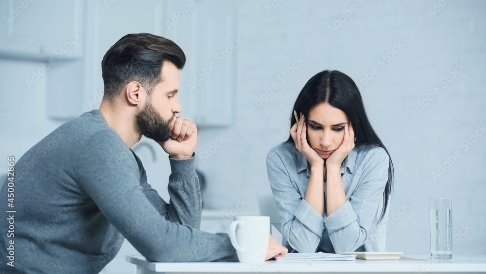 sad woman looking at calculator while sitting with upset man at home sad woman looking at calculator while sitting with upset man at home