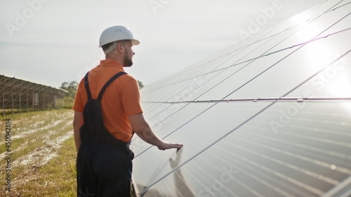 Professional male engineer in protective helmet walk on ecological solar plant construction. Concept of electricity, ecology, technologies. Farm of solar panels. Clean energy production. Green energy