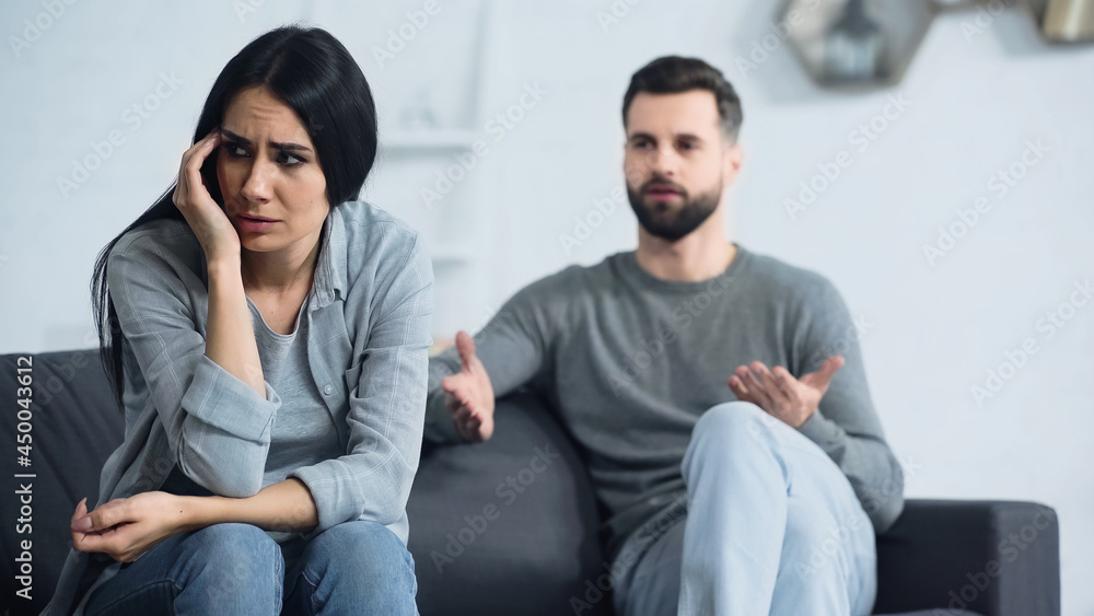 miserable woman sitting near blurred and displeased boyfriend quarrelling in living room