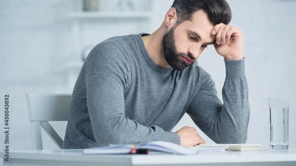 displeased man puffing cheeks and looking at calculator on table displeased man puffing cheeks and looking at calculator on table