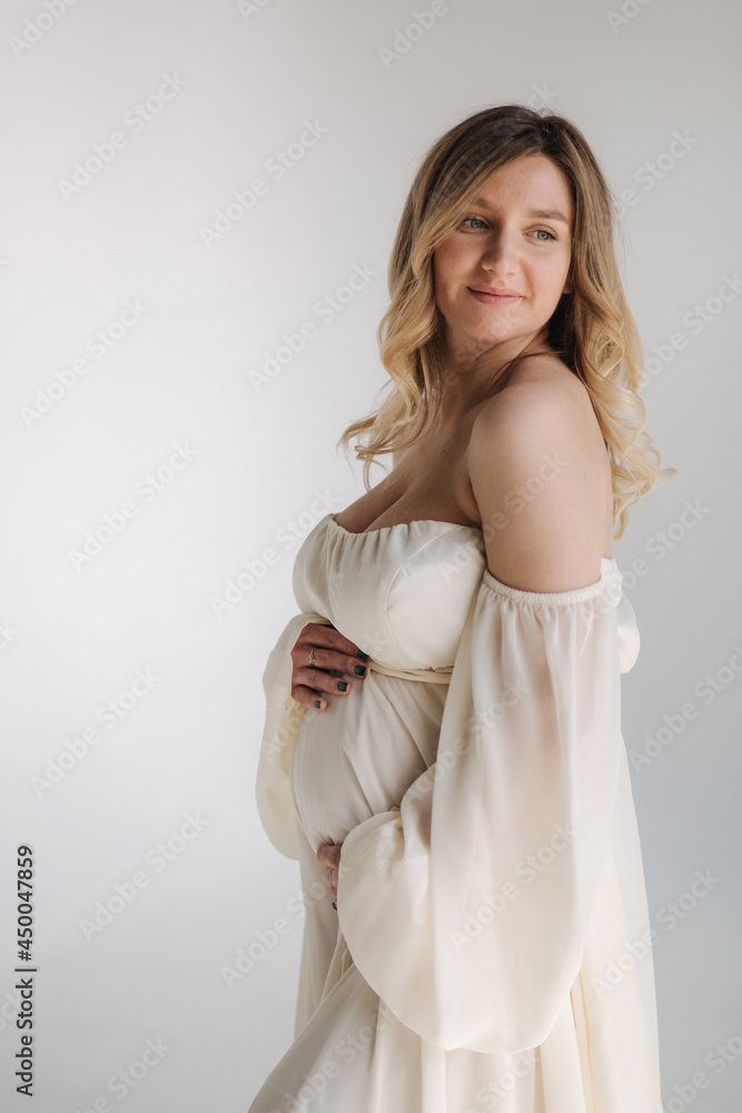 Beautiful portrait of pregnant woman in white dress. Concept of perfect pregnancy. Woman put her hand on belly. Future mother is waiting for baby Beautiful portrait of pregnant woman in white dress. Concept of perfect pregnancy. Woman put her hand on belly. Future mother is waiting for baby