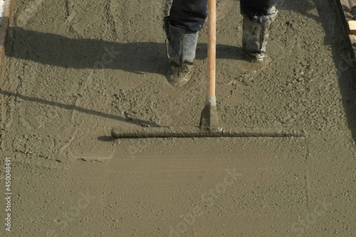 Construction works when filling the floor or foundation of the building.Builder mason worker leveling concrete with long trowel on construction site. He is standing in liquid concrete in his boots. photo