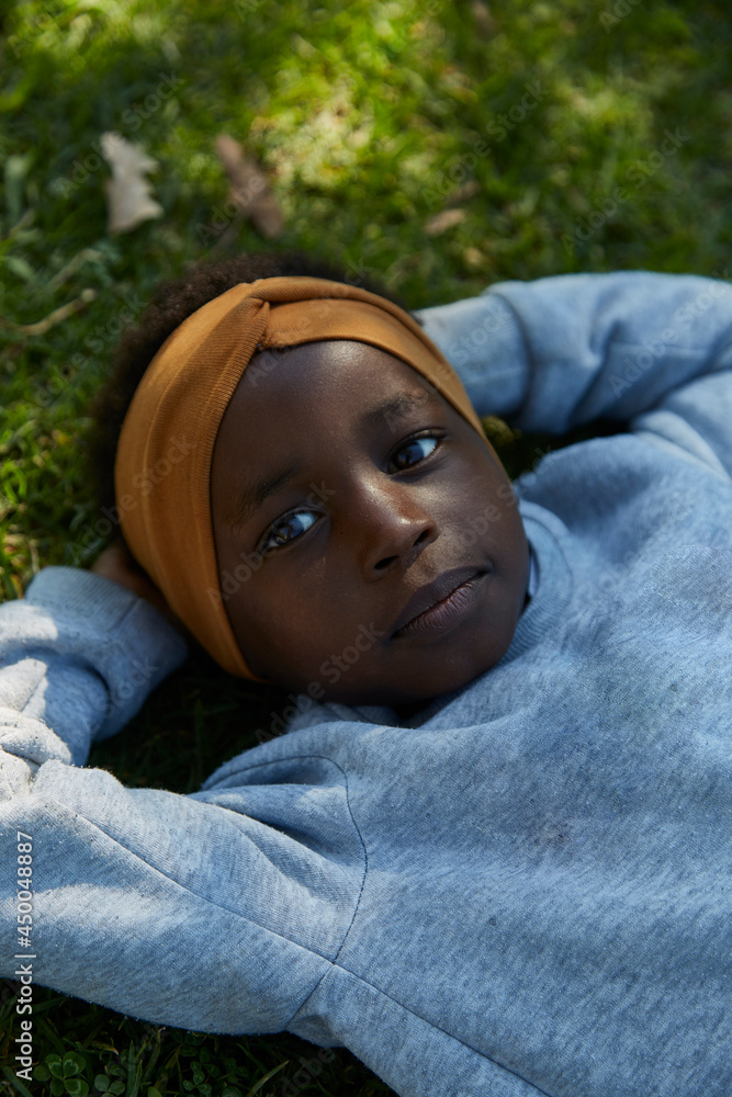 Pretty young black girl lying on grass in grey tracksuit. Pretty young black girl lying on grass in grey tracksuit.
