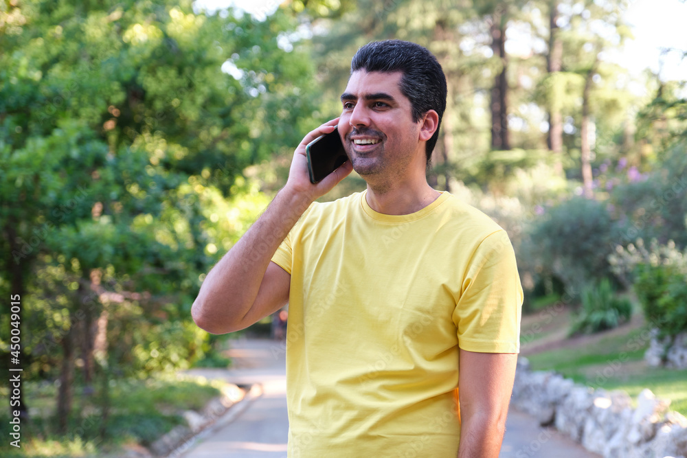 Man smiling and talking on the phone standing in a park. Man smiling and talking on the phone standing in a park.